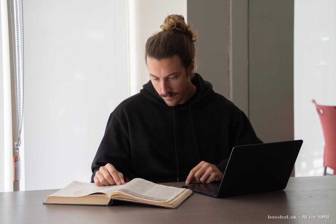 Man reads a book while using his laptop.